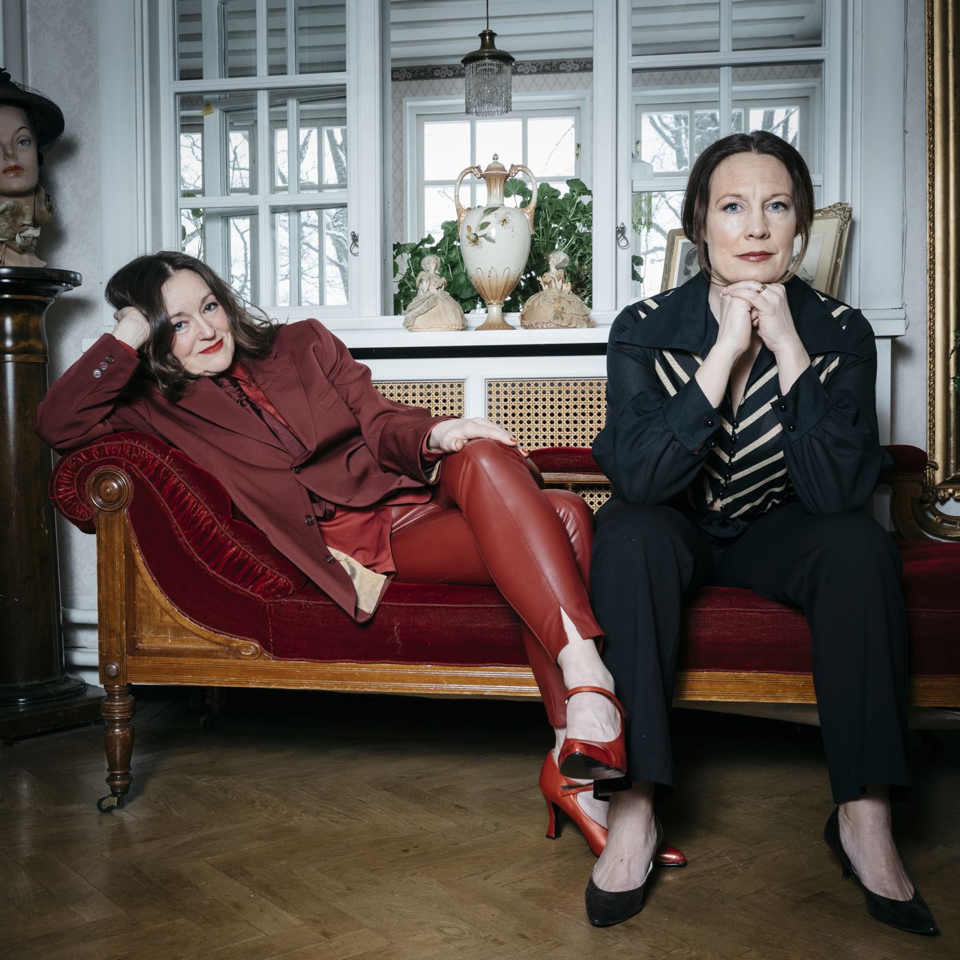 Julia och Yohanna sitter på en röd schäslong framför ett fönster